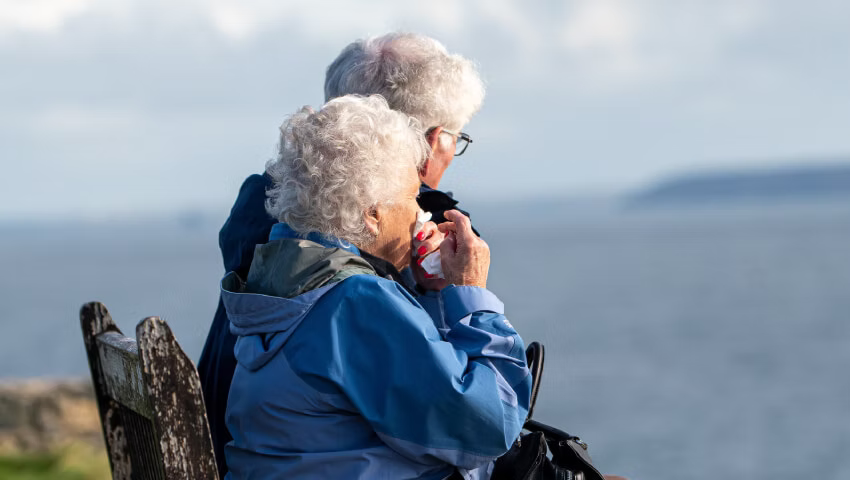 Caregiver holding a phone showing an older person's location on a map next to a compact Tack GPS tracker